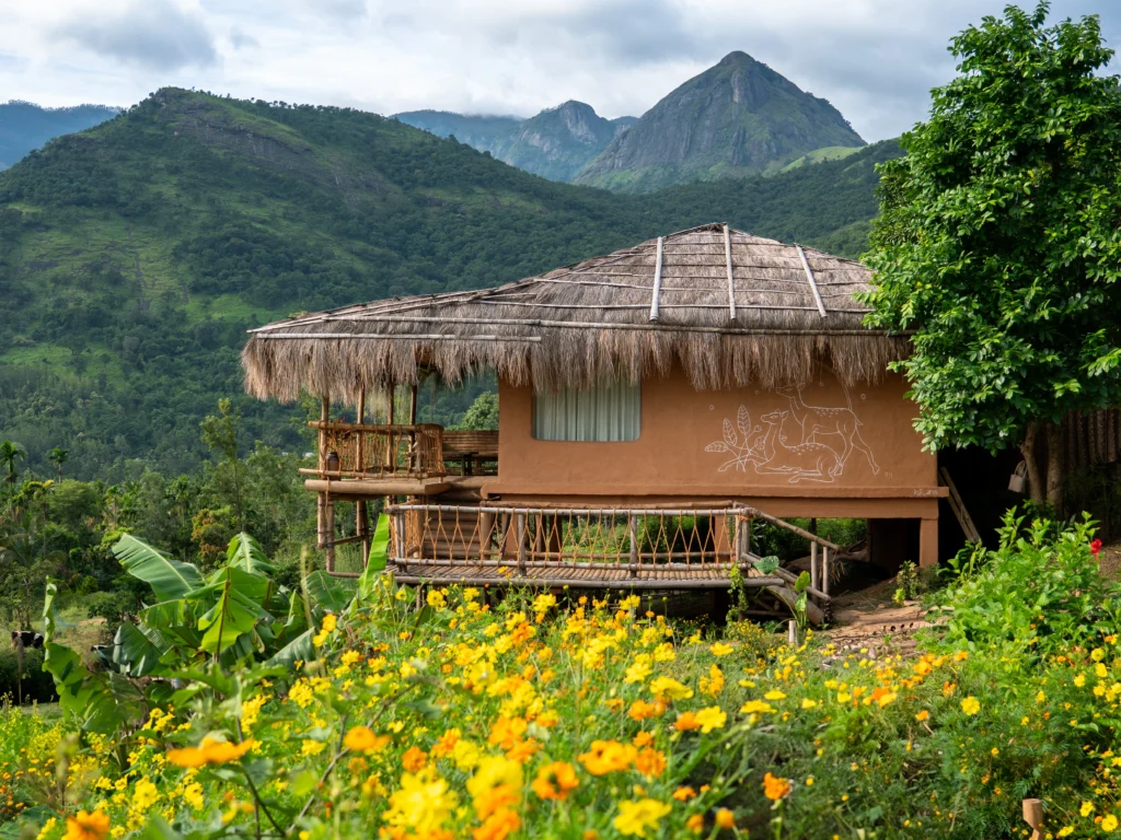 Traditional rural homestay surrounded by yellow flowers and green mountains in India.